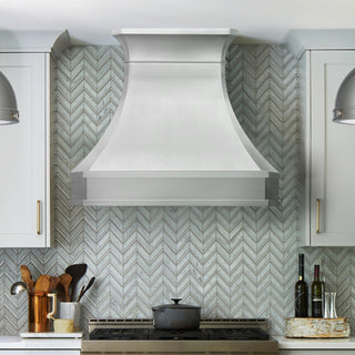 Kitchen with a large white range hood above a stove, featuring a chevron patterned backsplash.