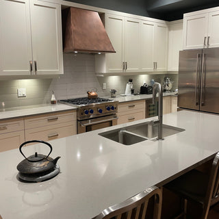 Modern kitchen with white countertops, copper range hood, and wooden cabinets.