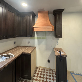 Kitchen with natural copper range hood and dark cabinets under construction
