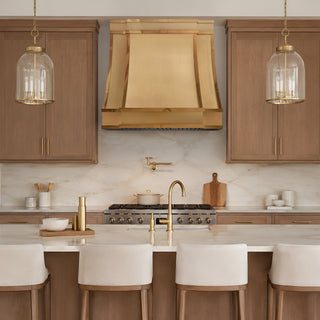 custom brushed brass stove vent hood witih polished straps in a luxury kitchen