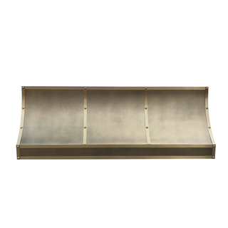 Front view of an aged brass range hood: Elongated profile with curved bottom edges; brushed brass straps with round rivets.