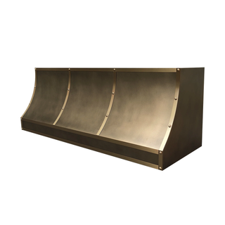 Right angled view of an aged brass kitchen hood: Elongated shape with curved bottom; brushed brass straps adorned with round rivets.