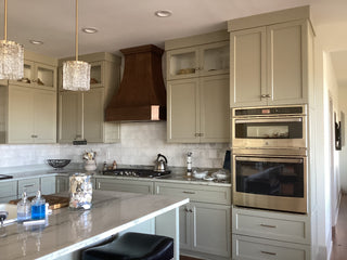 Modern kitchen with copper range hood beige cabinets, stainless steel appliances, and decorative lights.