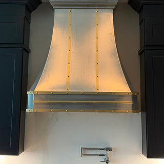 a stainless steel range hood with brass accents mounted between dark charcoal kitchen cabinets on a light gray wall