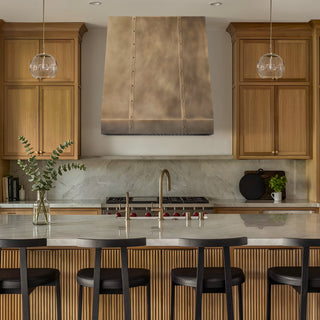 Modern kitchen with wooden cabinets, aged brass range hood, and a marble island.