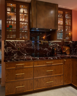 Modern kitchen with wooden cabinets, marble backsplash, and elegant aged brass ragne hood