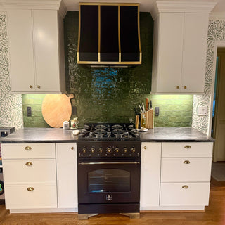 Modern kitchen with black stove and hood, white cabinets, and green backsplash.