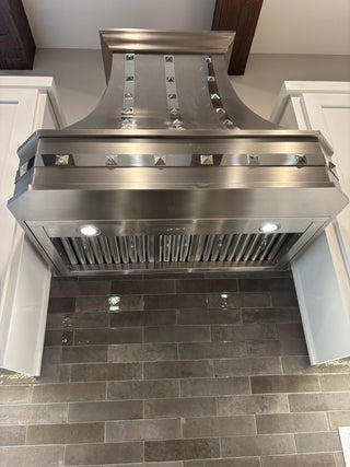 a stainless steel range hood mounted above a gray tiled kitchen backsplash, shown from a high-angle perspective between white cabinets