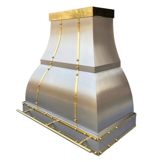 Side-angle view of a vent hood: Brushed stainless steel construction accented with brushed brass straps and rivets. It features a stepped silhouette—broad at the top, flaring outward mid-section, and narrowing at the base.