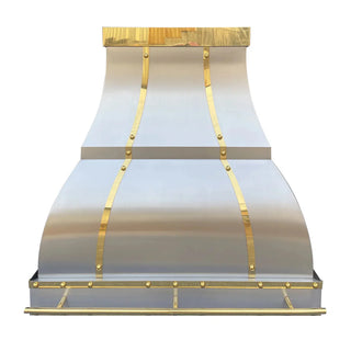 Front view of a kitchen hood: Brushed stainless steel body with brushed brass straps and rivets. Its shape widens at the top, curves outward in the middle, then tapers slightly toward the bottom.