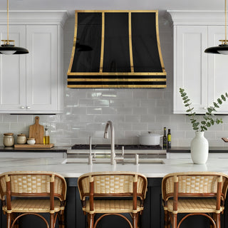 A modern kitchen scene featuring a black stainless steel range hood with brass straps.